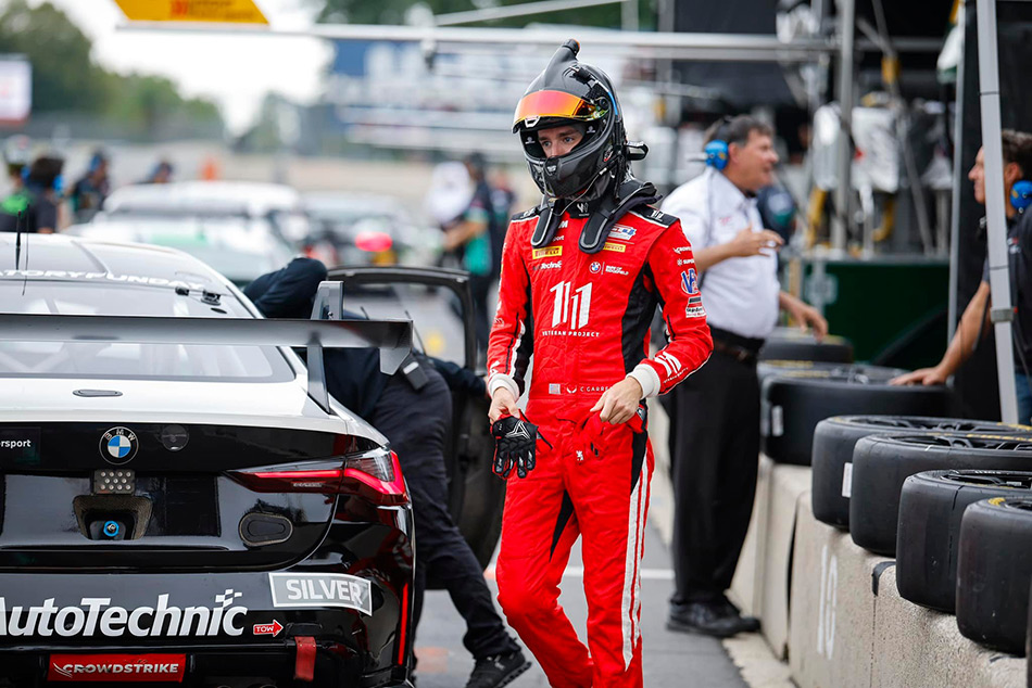 racecar driver Colin Garrett wearing a helmet & walking around his car on the track at Road America